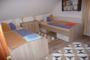 Una habitación pequeña con dos literas, un escritorio, una estantería y una alfombra estampada.