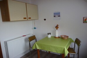 A dining area with a green tablecloth, chairs, a radiator, a cabinet, and a calendar on the wall. - Holiday apartment with 2 bedrooms (Sehestedt)