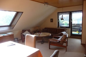 A cozy room with a sloped ceiling, a round table, a sofa, and a window with a view of the outdoors. - Holiday apartment with 2 bedrooms (Sehestedt)