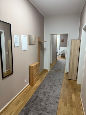 A hallway with a wooden floor, a grey carpet, a wooden dresser, and a mirror on the wall. - Apartment '4' with Wi-Fi (Erfurt)