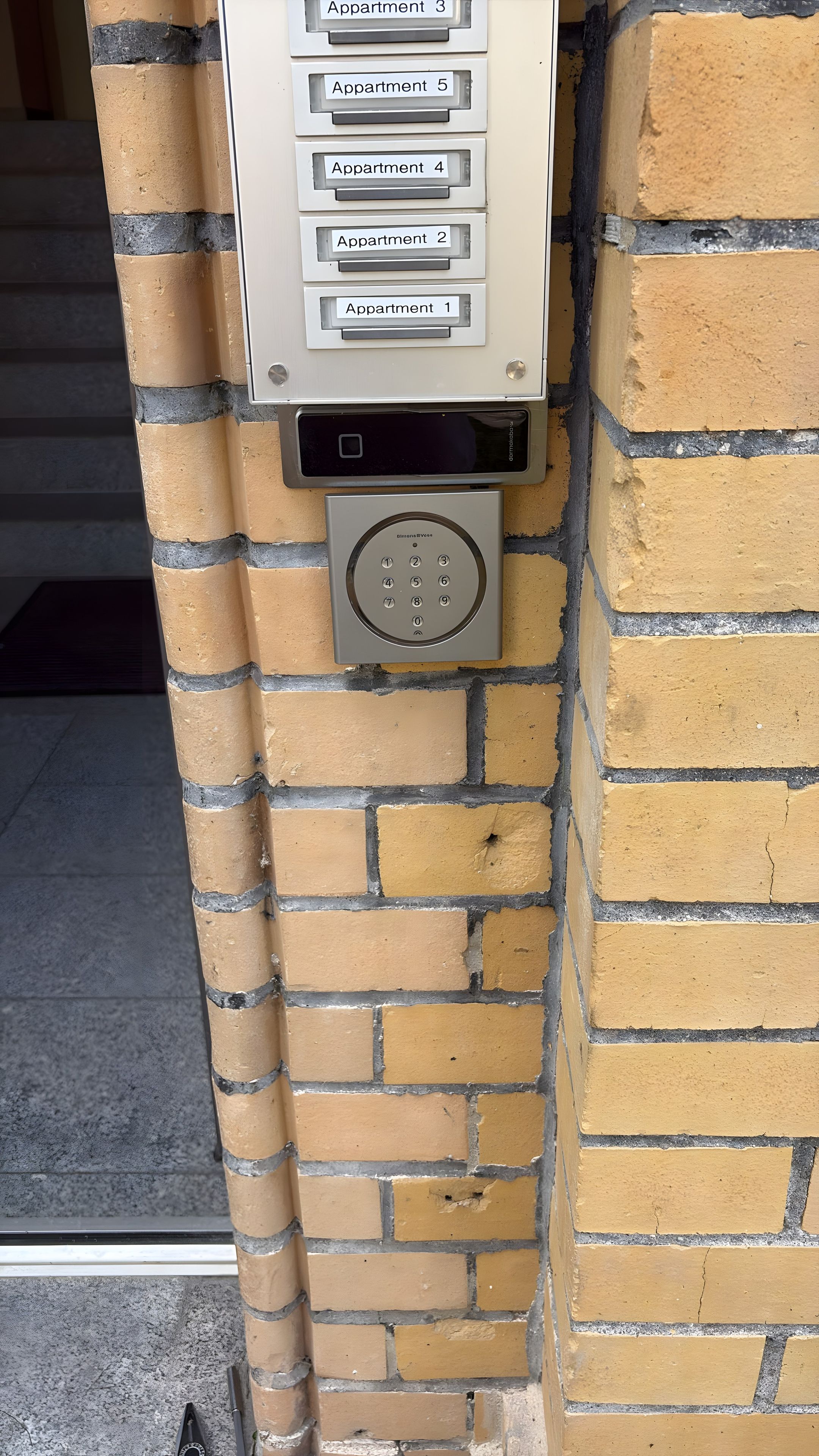 Ein an der Wand montiertes Gegensprechanlage mit beschrifteten Tasten für verschiedene Wohnungen.