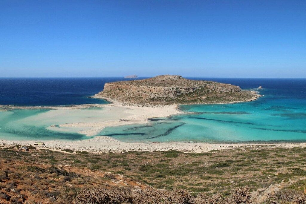 A coastal landscape with a rocky island, clear turquoise waters, and a sandy beach.