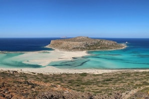 Eine Küstenlandschaft mit einer felsigen Insel, klarem türkisblauem Wasser und einem Sandstrand.