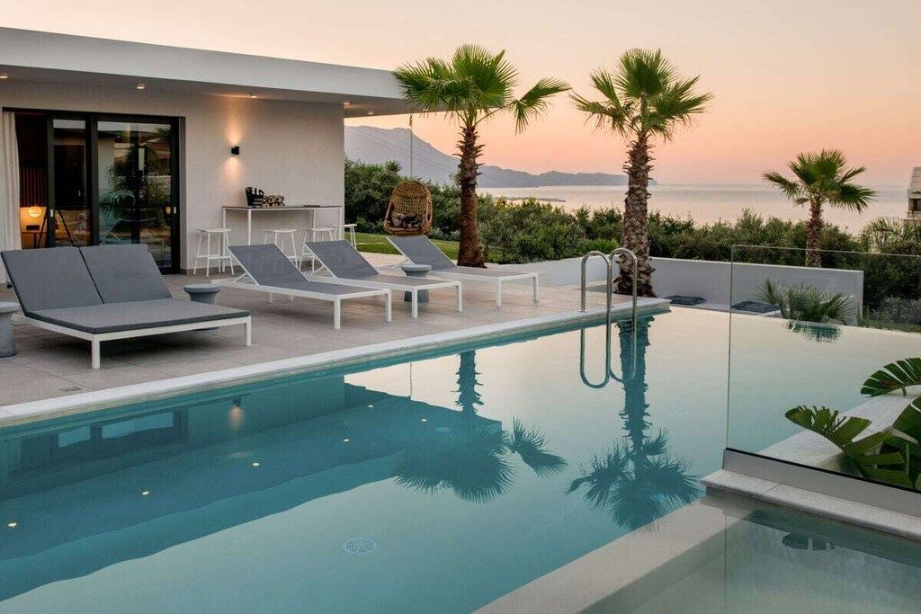 Ein moderner Poolbereich im Freien mit Liegestühlen und einem überdachten Pool, mit Blick auf ein Gewässer und Palmen.
