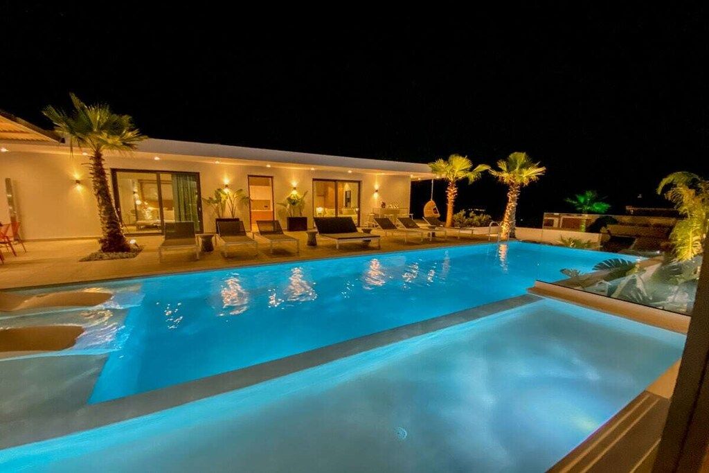 Una piscina con sillas de descanso y palmeras, rodeada por un edificio con ventanas y puertas.