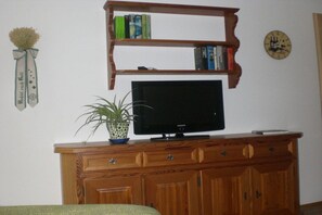 Ein Holzunterhaltungsschrank mit einem Flachbildfernseher, ein Bücherregal mit Büchern, eine Topfpflanze und eine Wanduhr.