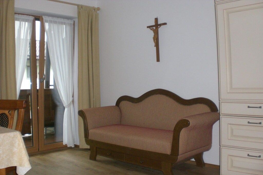 A room with a wooden sofa, a wooden cross on the wall, and a sliding glass door with curtains.