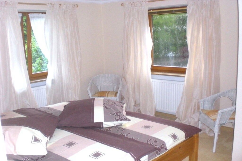 A bedroom with a bed, two chairs, and a window with curtains.