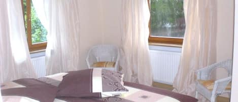 Une chambre à coucher avec un lit, deux chaises et une fenêtre avec des rideaux.