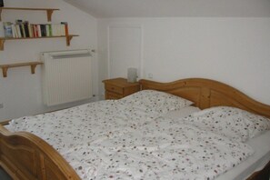Ein Schlafzimmer mit einem hölzernen Bett, einem Heizkörper, einem Nachttisch und einem Bücherregal mit Büchern.