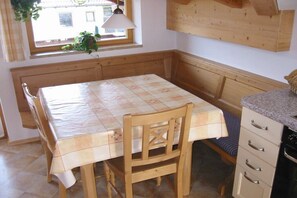 Eine Küche mit einem Holztisch, einer Bank, einem Fenster mit einer Pflanze und einem Schrank mit Schubladen.