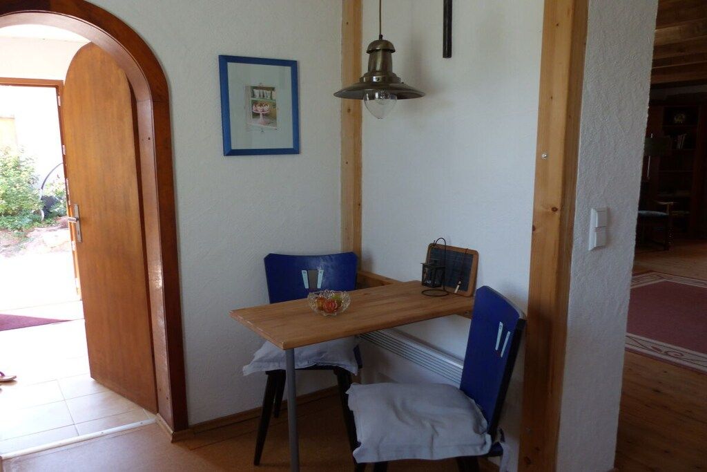 Un comedor con una mesa de madera, dos sillas azules, una lámpara colgante y un cuadro en la pared.