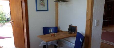Un comedor con una mesa de madera, dos sillas azules, una lámpara colgante y un cuadro en la pared.