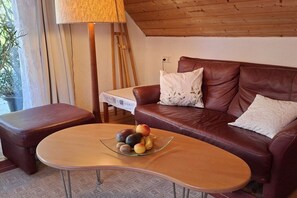 Ett mysigt vardagsrum med en brun lädersoffa, ett glasbord med frukt på och en lampa.
