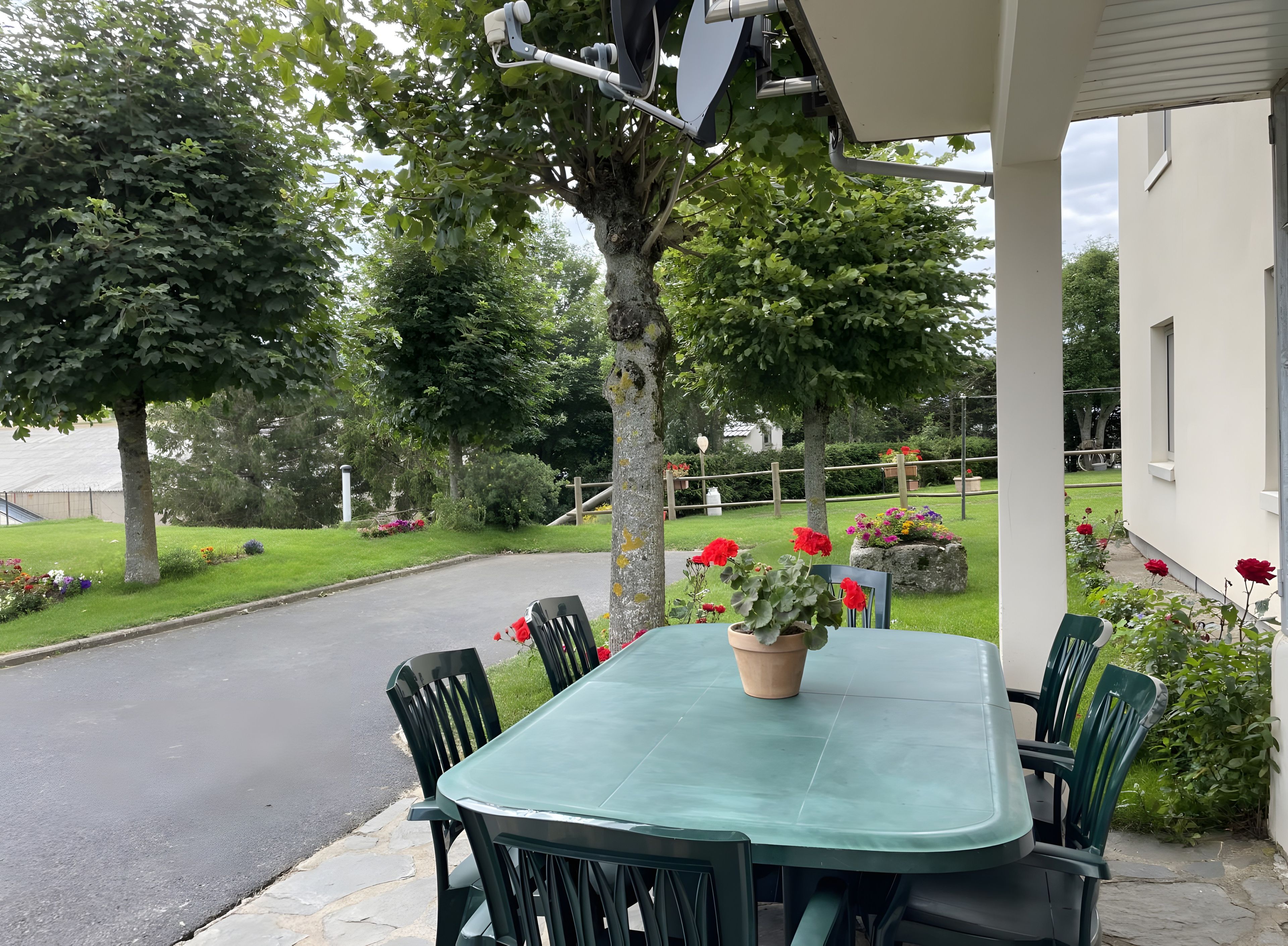 An outdoor patio with a table and chairs, surrounded by greenery and a pathway.