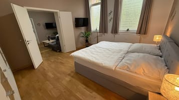 Een slaapkamer met een bed, een televisie, een raam met gordijnen en een plant.