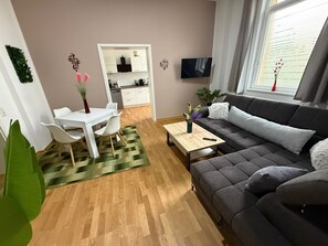 A modern living room with a grey sofa, a dining table with chairs, a kitchen area, and a large window with curtains. - Apartment '5' with Wi-Fi (Erfurt)