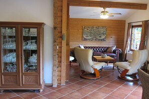 A room with a wooden cabinet, leather sofa, two armchairs, a coffee table, and a ceiling fan. - Heideblockhaus Harmonie (Neuenkirchen)
