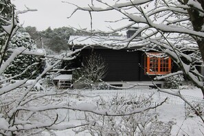 A snow-covered house with a fenced yard and a visible garage door. - Heideblockhaus Harmonie (Neuenkirchen)