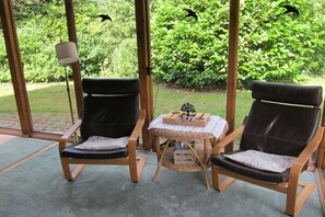Two black leather chairs with cushions, a small wicker table with a tray, and a lamp. - Heideblockhaus Harmonie (Neuenkirchen)