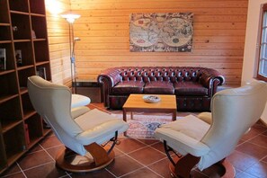 A cozy room with a leather sofa, two armchairs, a wooden bookshelf, a globe wall art, and a floor lamp. - Heideblockhaus Harmonie (Neuenkirchen)