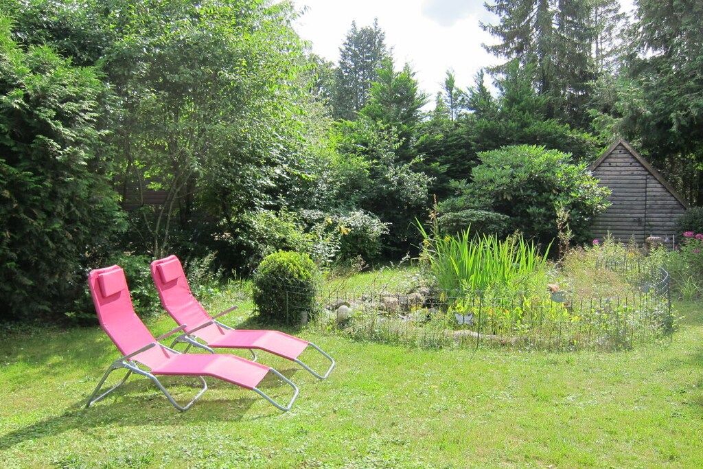 Ein Garten mit zwei rosafarbenen Liegestühlen, einer Holzkonstruktion und unterschiedlichen Pflanzen.