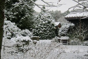 A snow-covered landscape with a large evergreen tree and a building with a sloped roof. - Heideblockhaus Harmonie (Neuenkirchen)