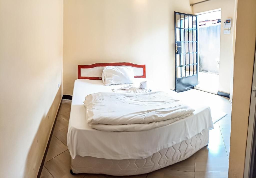 Un lit simple avec un matelas blanc et une tête de lit rouge, dans une pièce dont le sol est carrelé.