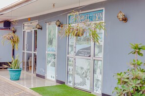 A hotel entrance with a sign reading 'WENYEI INN' and a 'LUXURY ACCOMODATION FULL AC FREE WIFI' sign. There are potted plants and a green mat at the entrance. - Wenyeji Inn  Hotel (Moshi)