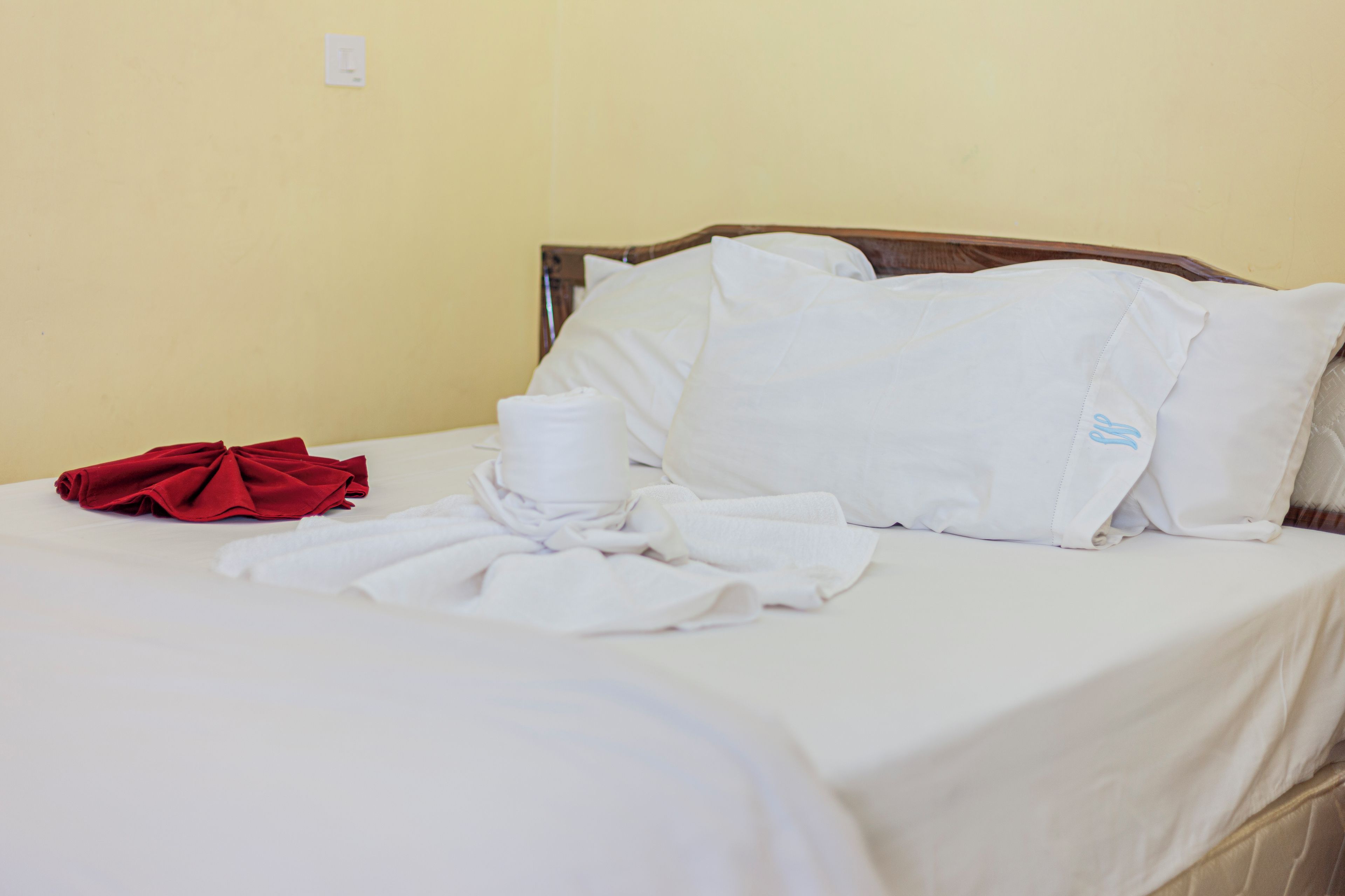 Una cama con ropa de cama blanca, una toalla roja y un cojín con logotipo azul.