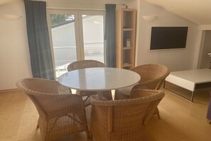 A dining area with a round table and wicker chairs, a bookshelf, a flat-screen TV, and a sliding glass door leading to an outdoor area. - Studio apartment Diessen (Diessen)