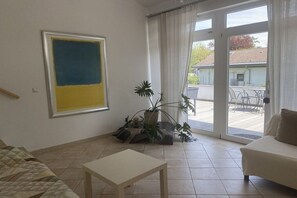 A living room with a sofa, a table, a large abstract painting, and a sliding glass door leading to an outdoor area. - Studio apartment Diessen (Diessen)
