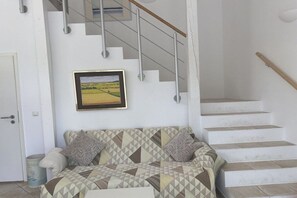 A living room with a sofa, a framed picture on the wall, and a staircase. - Studio apartment Diessen (Diessen)