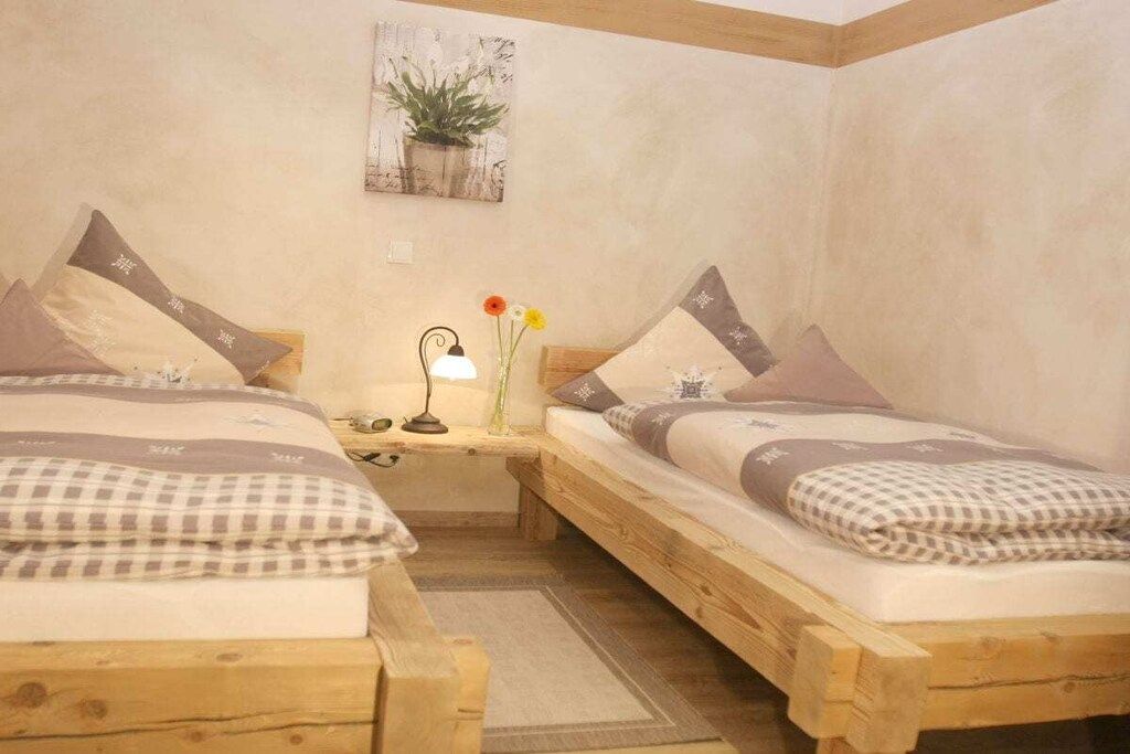 Un dormitorio con dos camas de madera, una mesita de noche con lámpara y una planta en la pared.