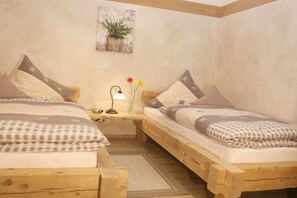 Ein Schlafzimmer mit zwei Holzbetten, einem Nachttisch mit Lampe und einer an der Wand befestigten Pflanze.