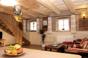 A rustic interior with a wooden staircase, a dining area with a fruit bowl, a sofa, and a table with bottles. - Holiday apartment with 1 bedroom (Freyung)