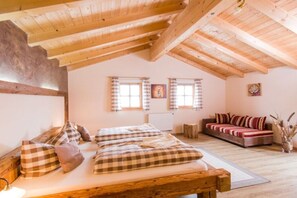 Une pièce avec un plafond en bois, un lit recouvert d’une couette à carreaux, un canapé et deux fenêtres avec des rideaux.