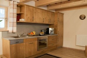 Une cuisine compacte avec des meubles en bois, un four encastré, une machine à café et une fenêtre agrémentée d’un rideau à rayures.