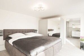 A modern bedroom with a large bed, bedside tables, and a mirror. - Holiday home Emmelsbüll (Emmelsbüll-Horsbüll)