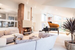 Un salon spacieux avec une cheminée, un piano et une grande fenêtre.
