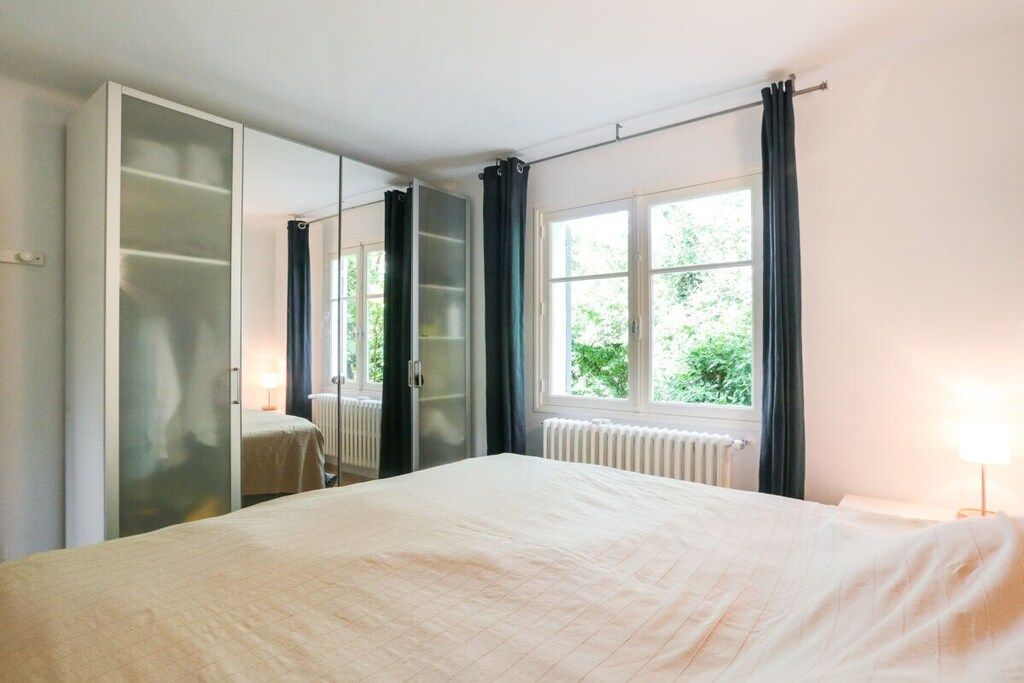 A bedroom with a bed, a wardrobe, a window with curtains, and a radiator.