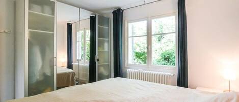 A bedroom with a bed, a wardrobe, a window with curtains, and a radiator.