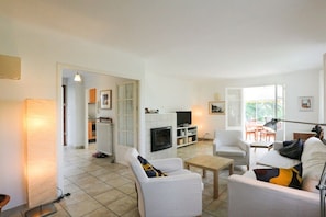 Ein Wohnzimmer mit Kamin, weißen Sofas, einem Fernseher und einem Essbereich mit Stühlen.