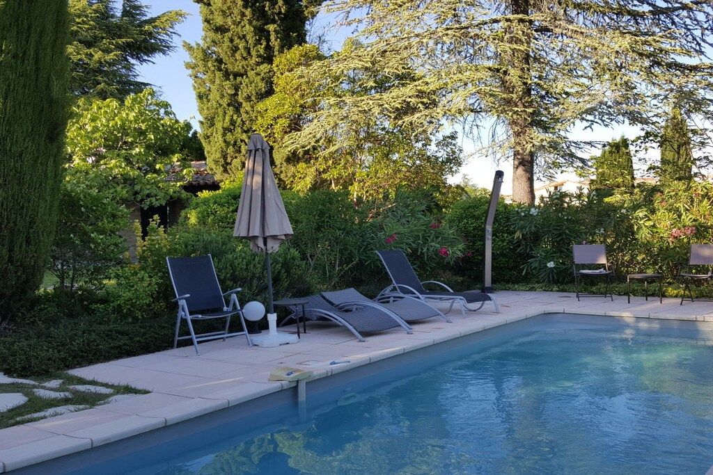 A swimming pool with lounge chairs and umbrellas, surrounded by greenery and trees.