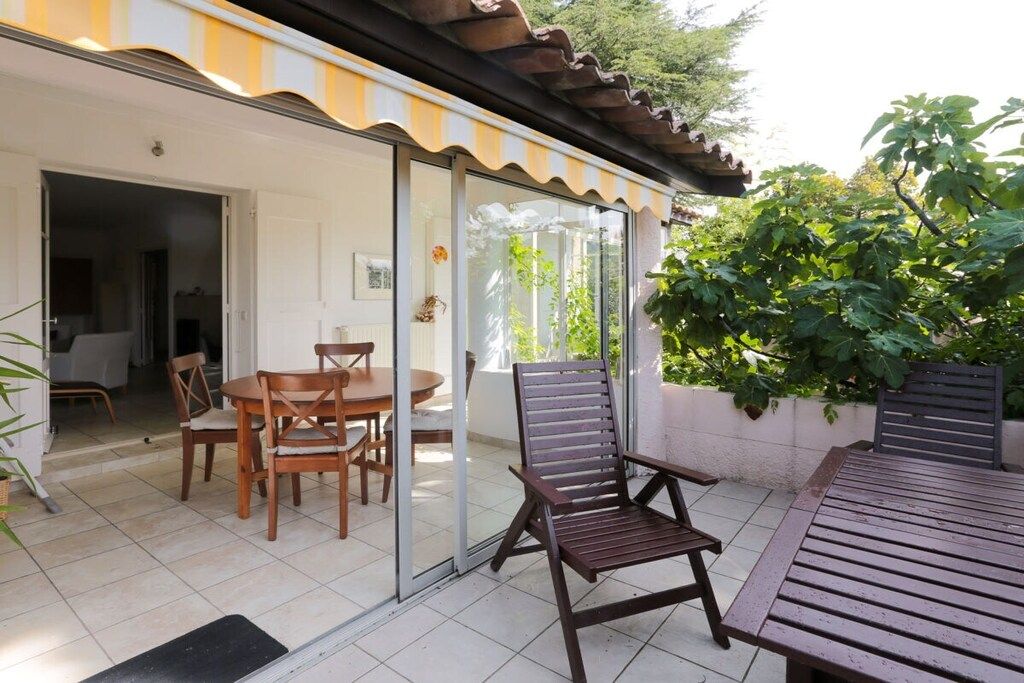 Eine Terrasse mit Tisch und Stühlen, eine hölzerne Bank und eine Glastür zu einem Innenbereich.