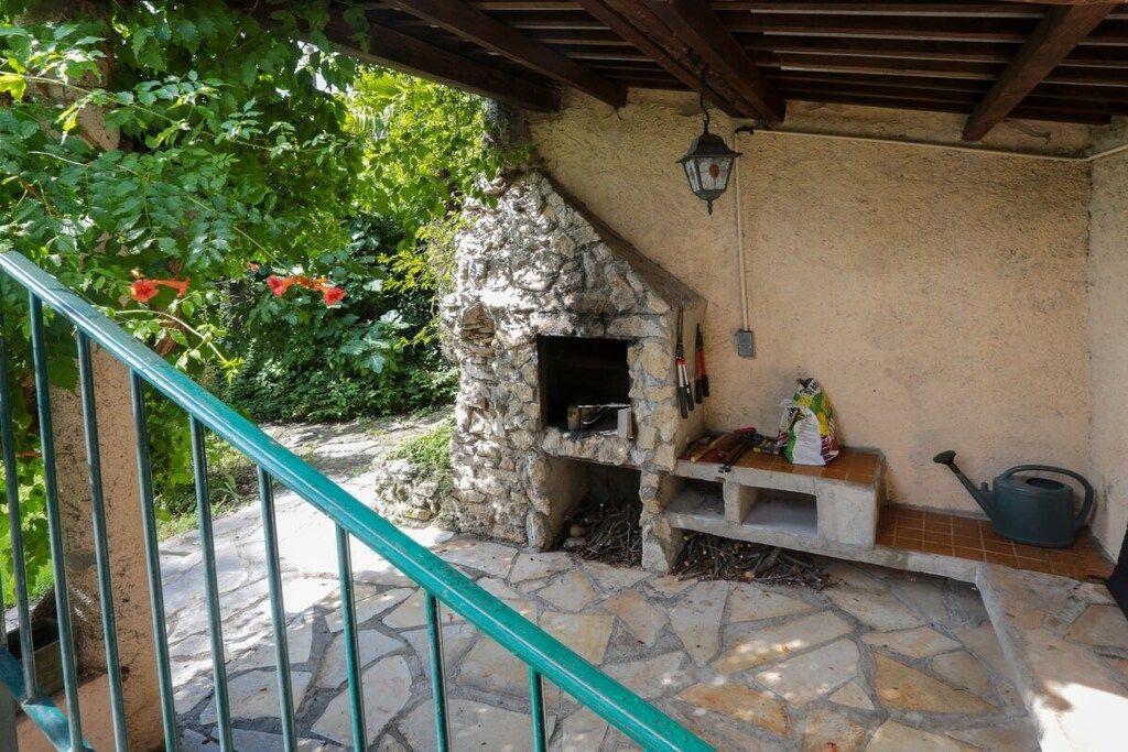 Un espace extérieur aménagé en pierre, doté d’un barbecue intégré, d’un banc en pierre et d’une rambarde en métal.