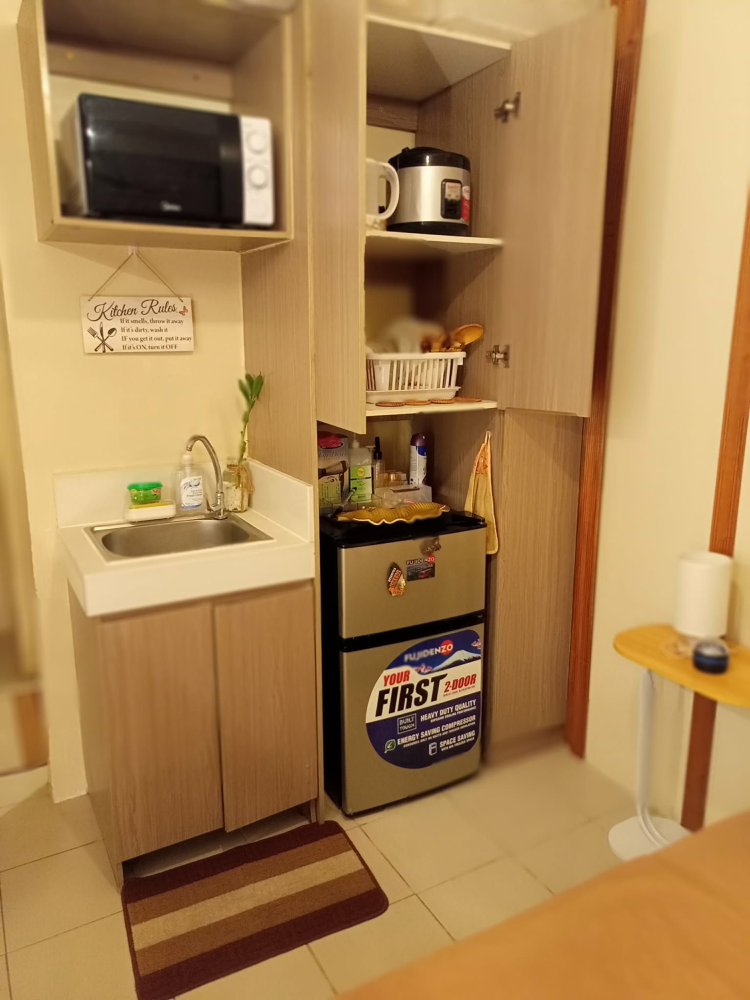 Una cocina compacta con un fregadero, un microondas, un refrigerador y una mesita con una taza.