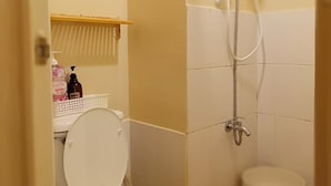 A bathroom with a toilet, a shower, and a shelf with toiletries.