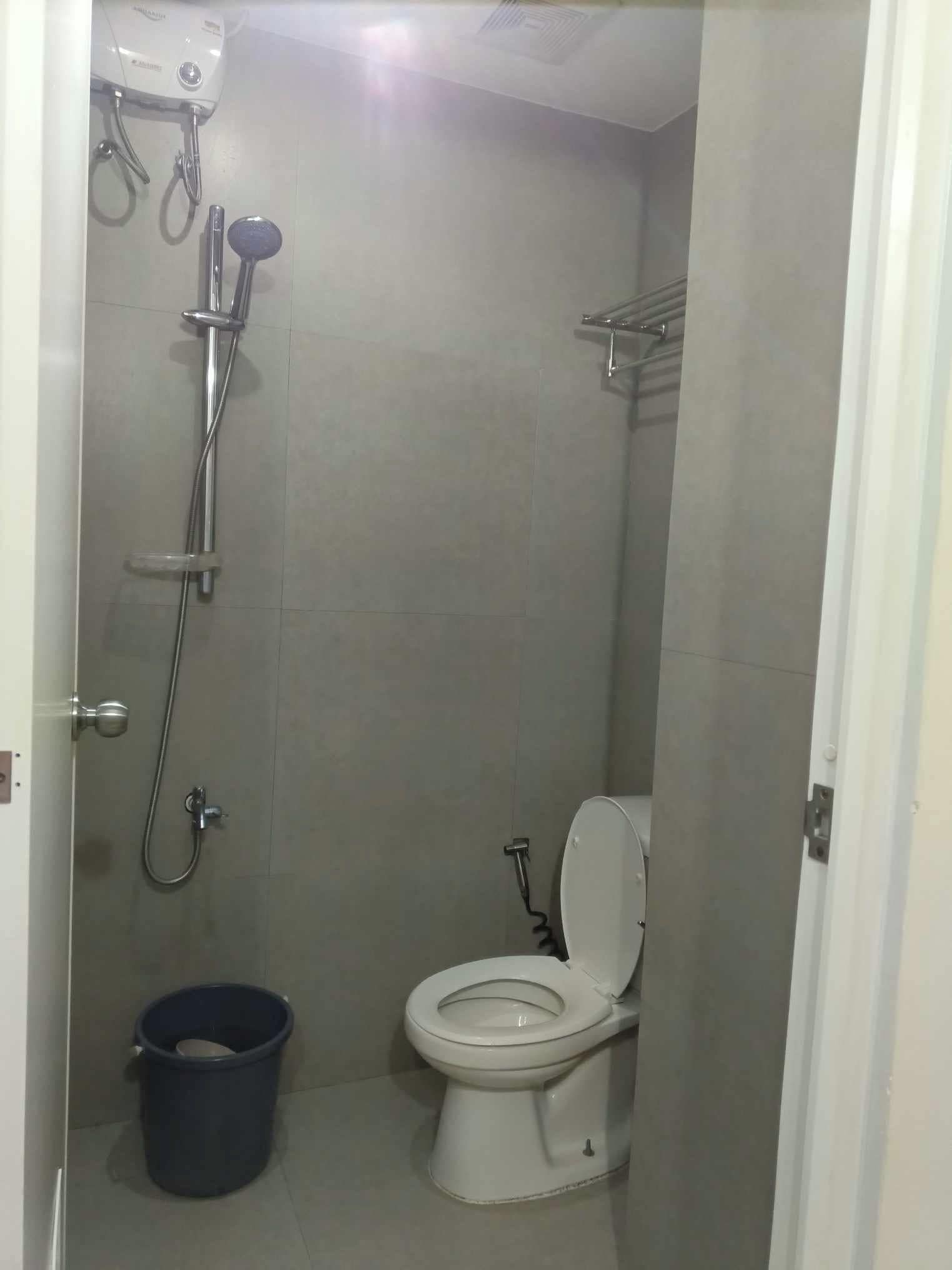 A small bathroom with a toilet, a shower, and a bucket.