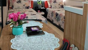 A compact room with a bed, a small table with a vase of flowers, and a window with curtains.